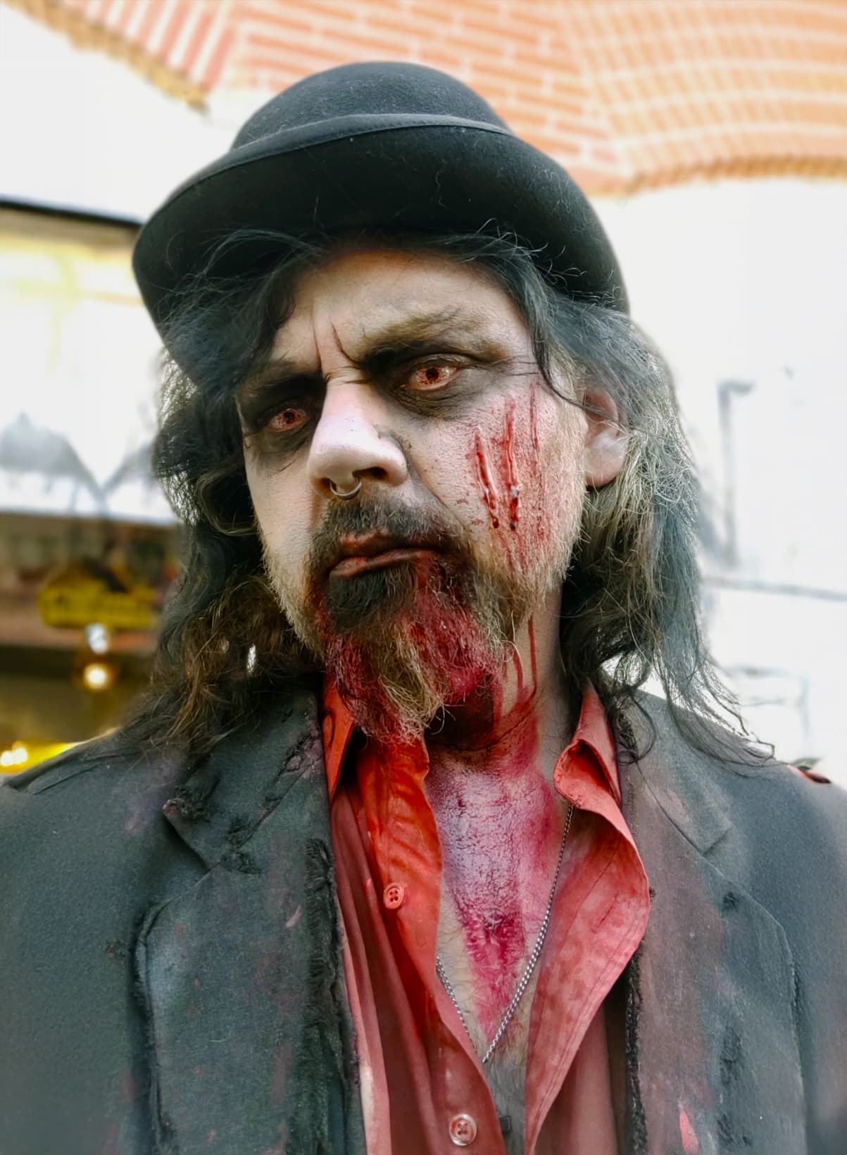Mayor Joseph character in a bowler hat, pale faced and bloodied, staring straight into the camera