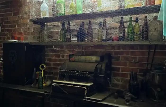 The speakeasy escape room, a dim prohibition-era bar behind a hidden door, bottles glinting in low light